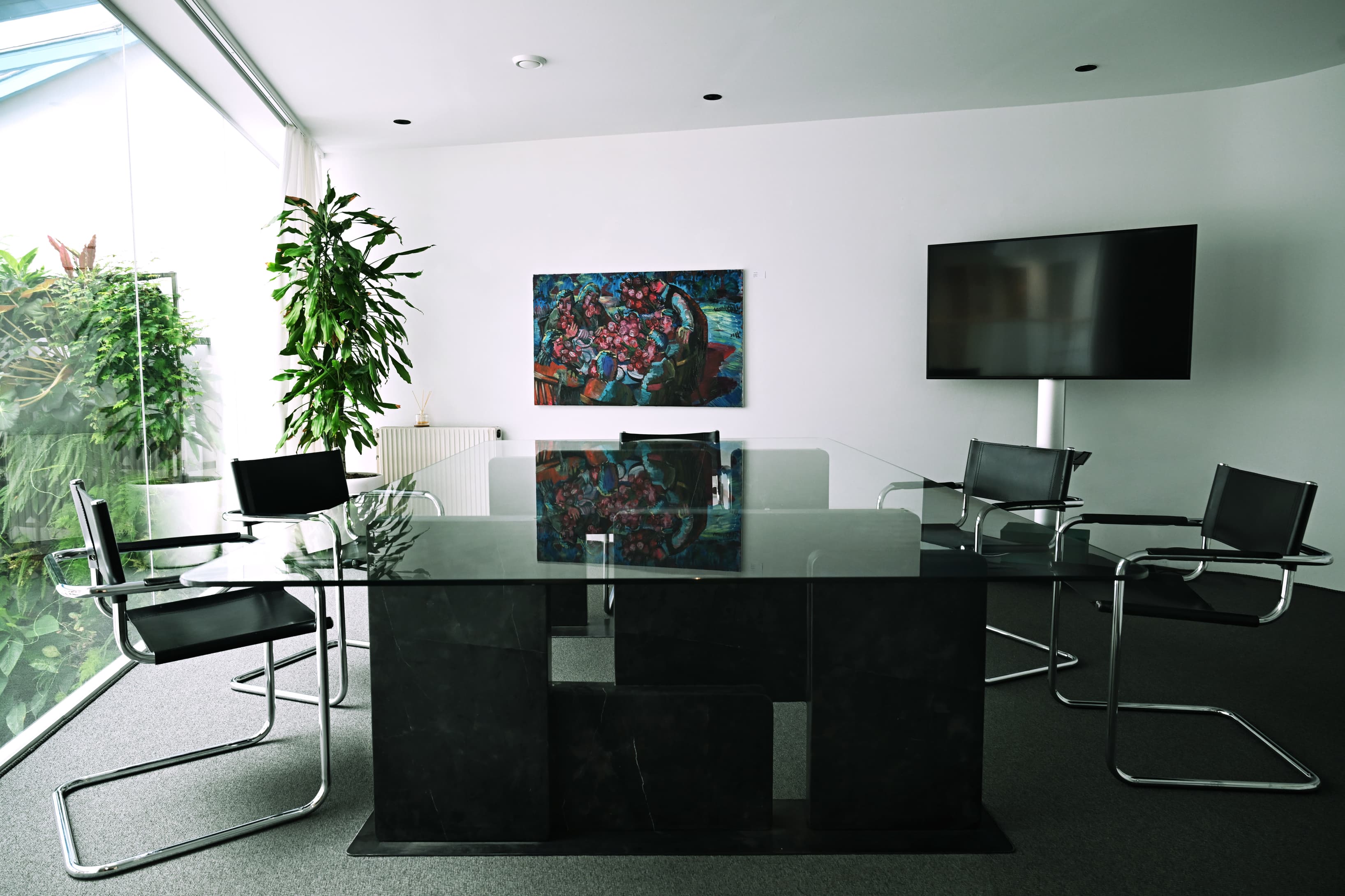 An elegant meeting suite centered around a sculptural glass art table with serene garden views.