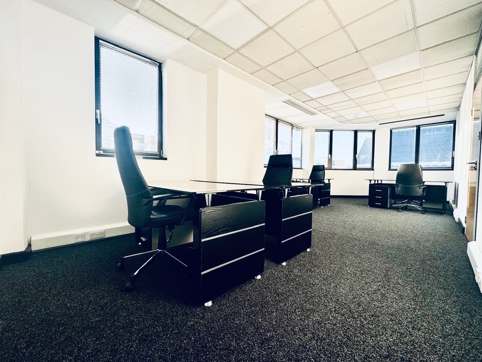 5 person spacious furnished office with large windows, desks and office chairs.