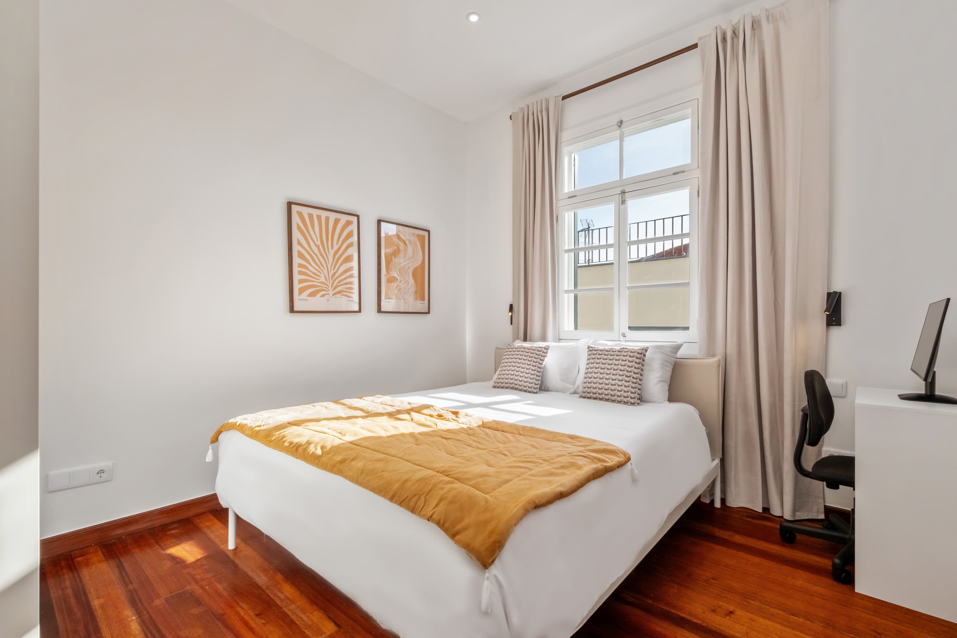 Bright and airy private bedroom featuring warm wooden floors, a comfortable bed with a mustard yellow throw, stylish wall art