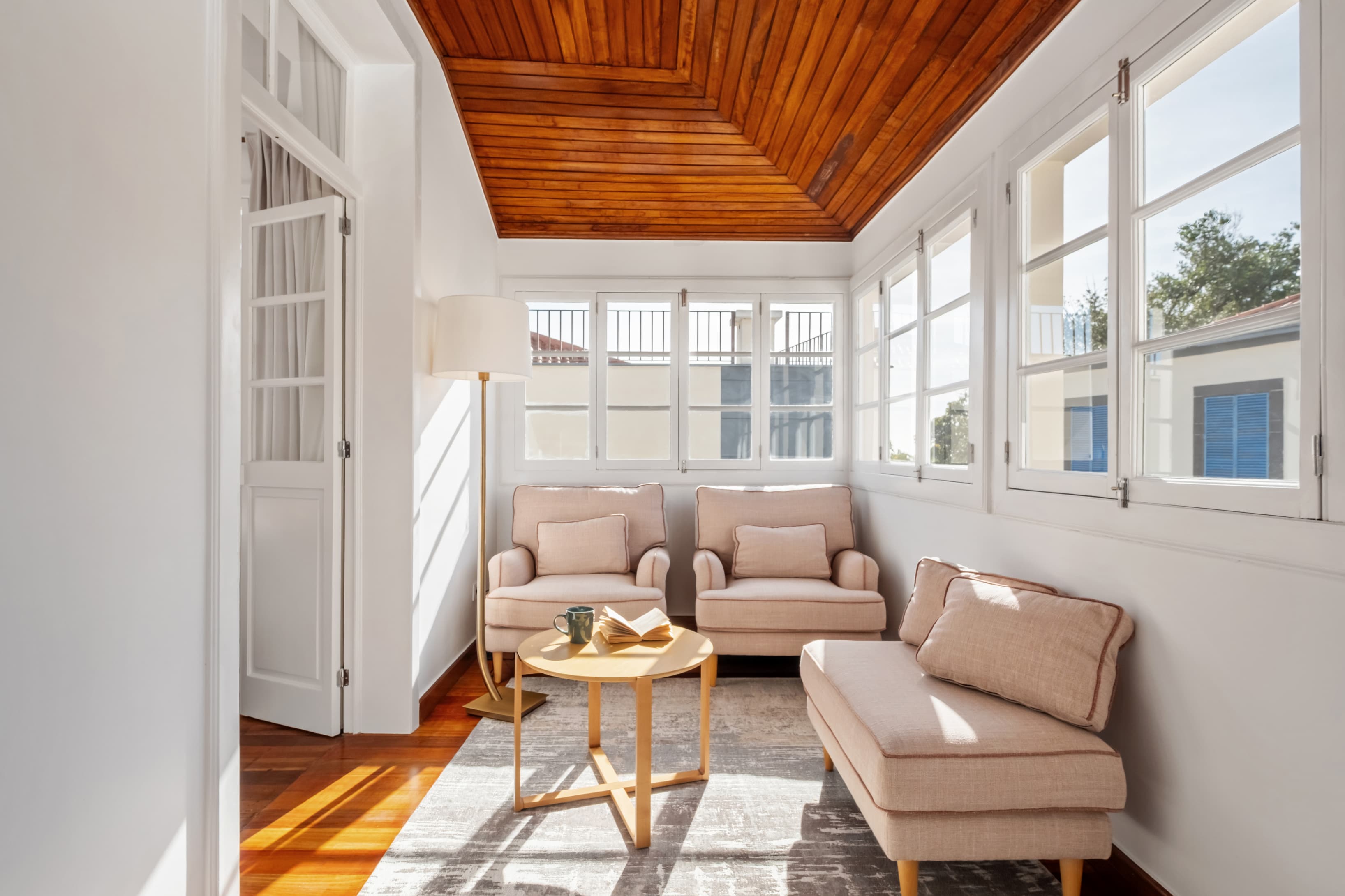 Bright and cozy sunlit lounge area with comfortable armchairs, warm wooden ceilings, and large windows.
