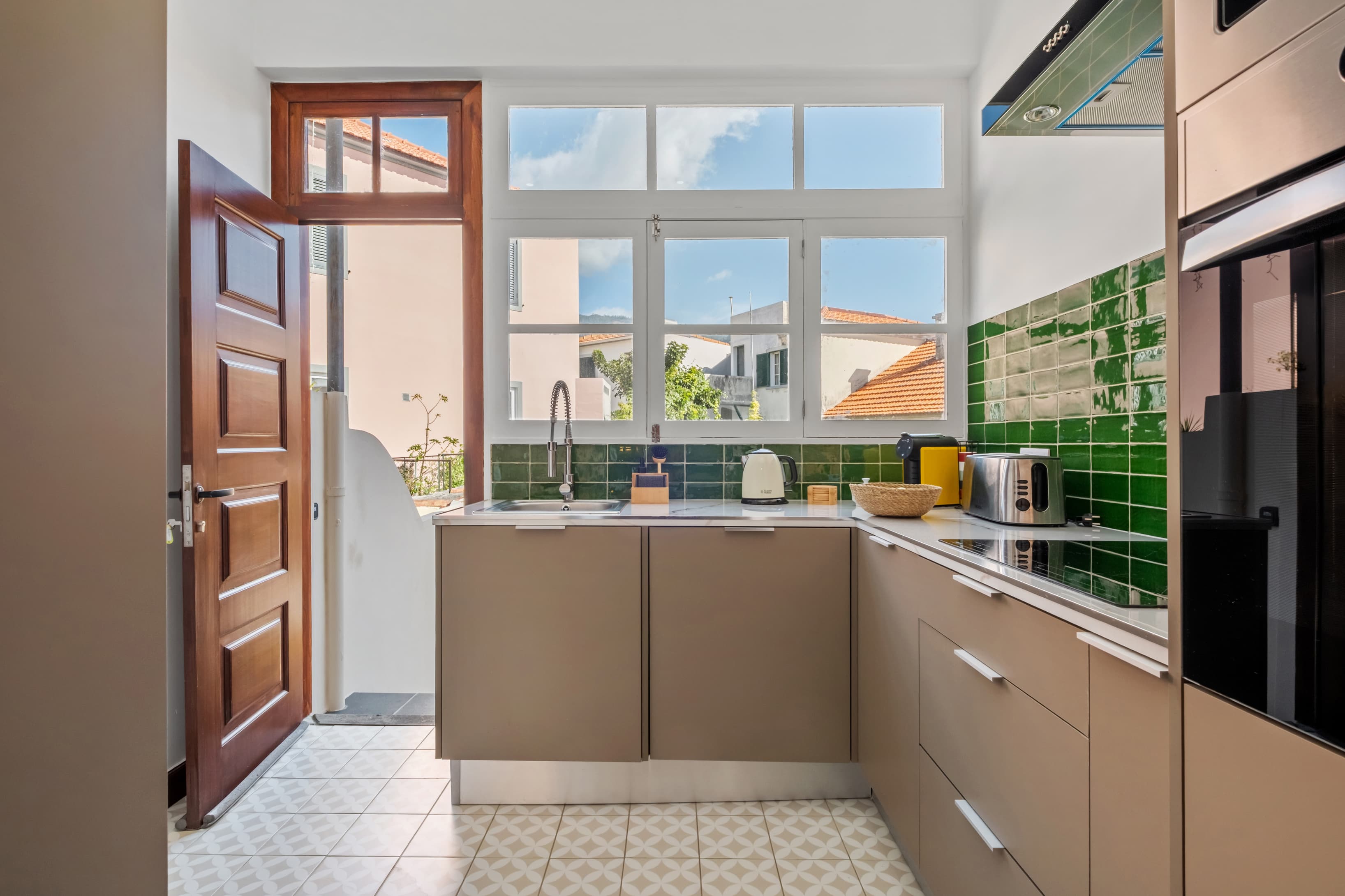 Bright, fully equipped kitchen area with modern appliances, green tile backsplash, and an open door to the outdoors.