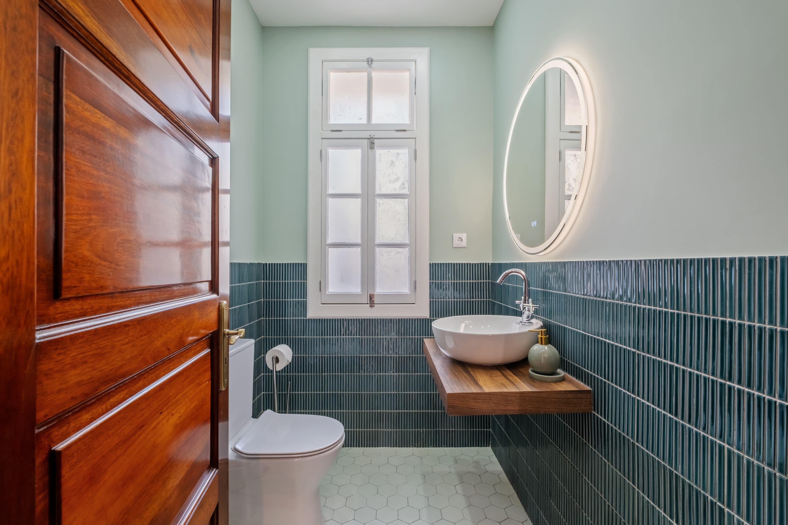 Modern bathroom featuring stylish deep green tiles, a floating wooden vanity, and an illuminated mirror.
