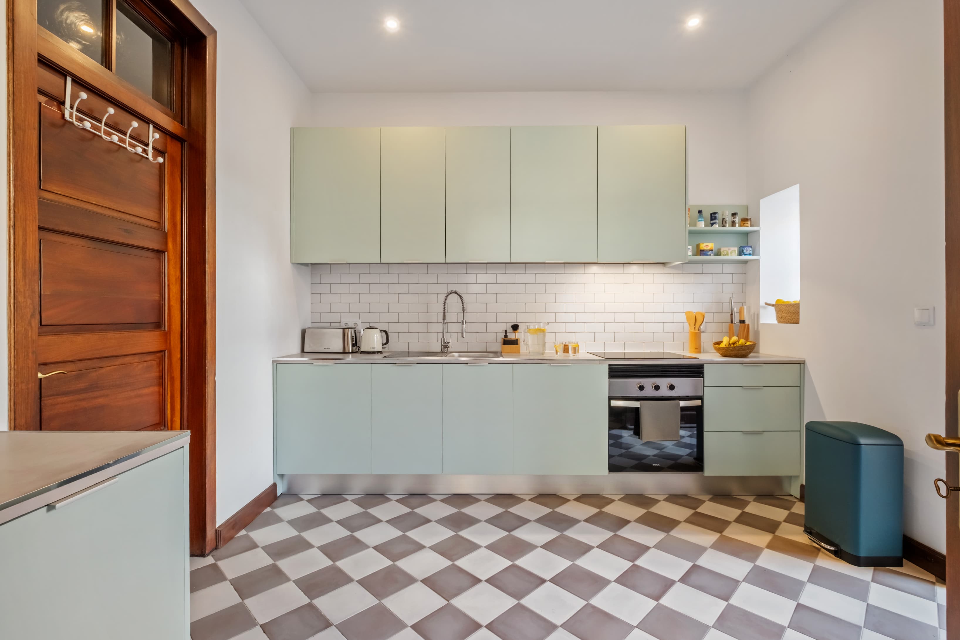 Fully equipped modern communal kitchen featuring sleek mint-green cabinets and a classic checkered floor.