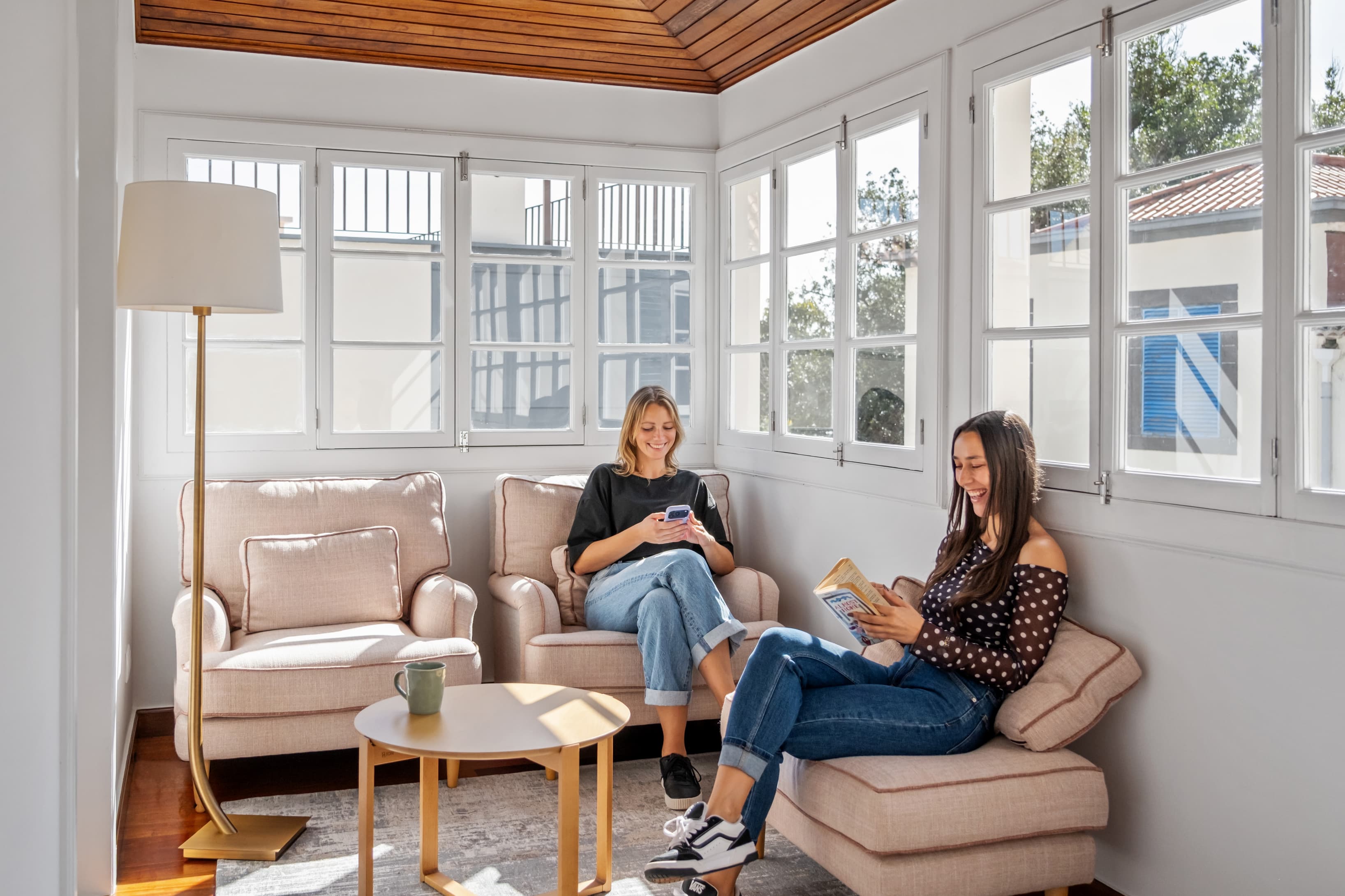 Community members relaxing, reading, and connecting in the bright and comfortable sunroom lounge.
