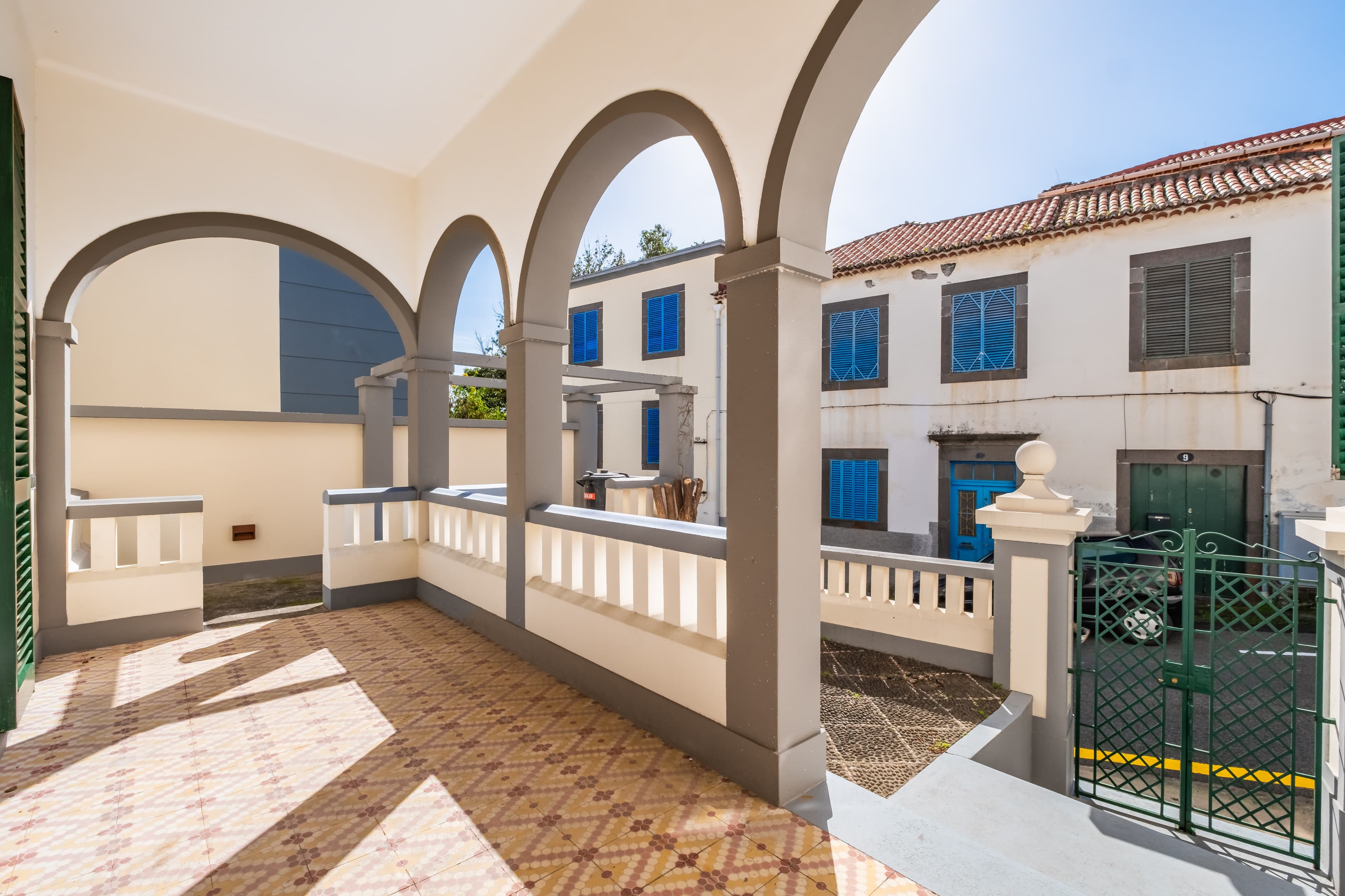 Covered outdoor balcony corridor with classic arches, patterned tiles, and traditional blue doors.