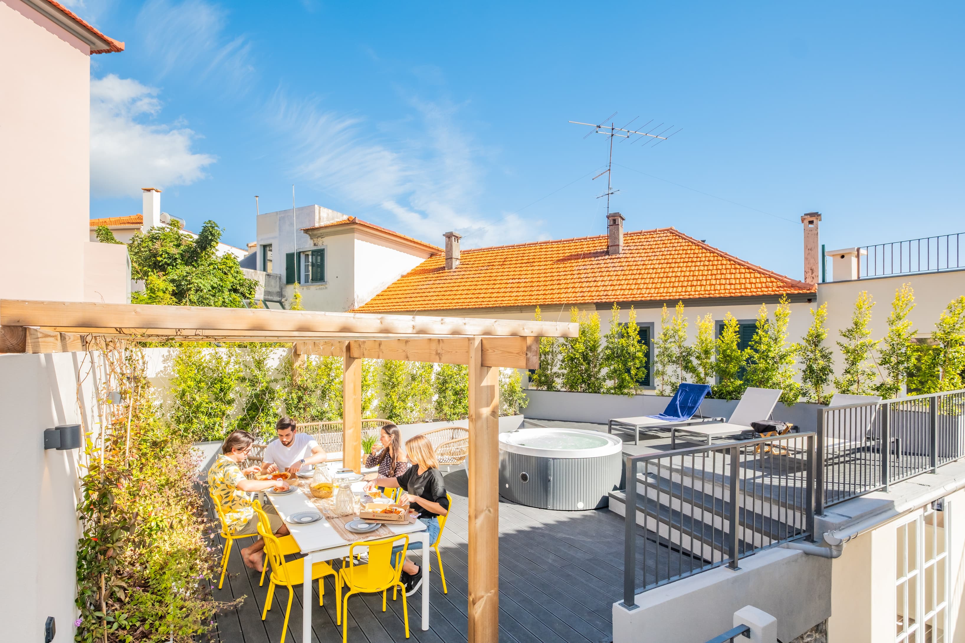 Beautiful outdoor wooden terrace featuring a shared dining table, sun loungers, and a relaxing jacuzzi.