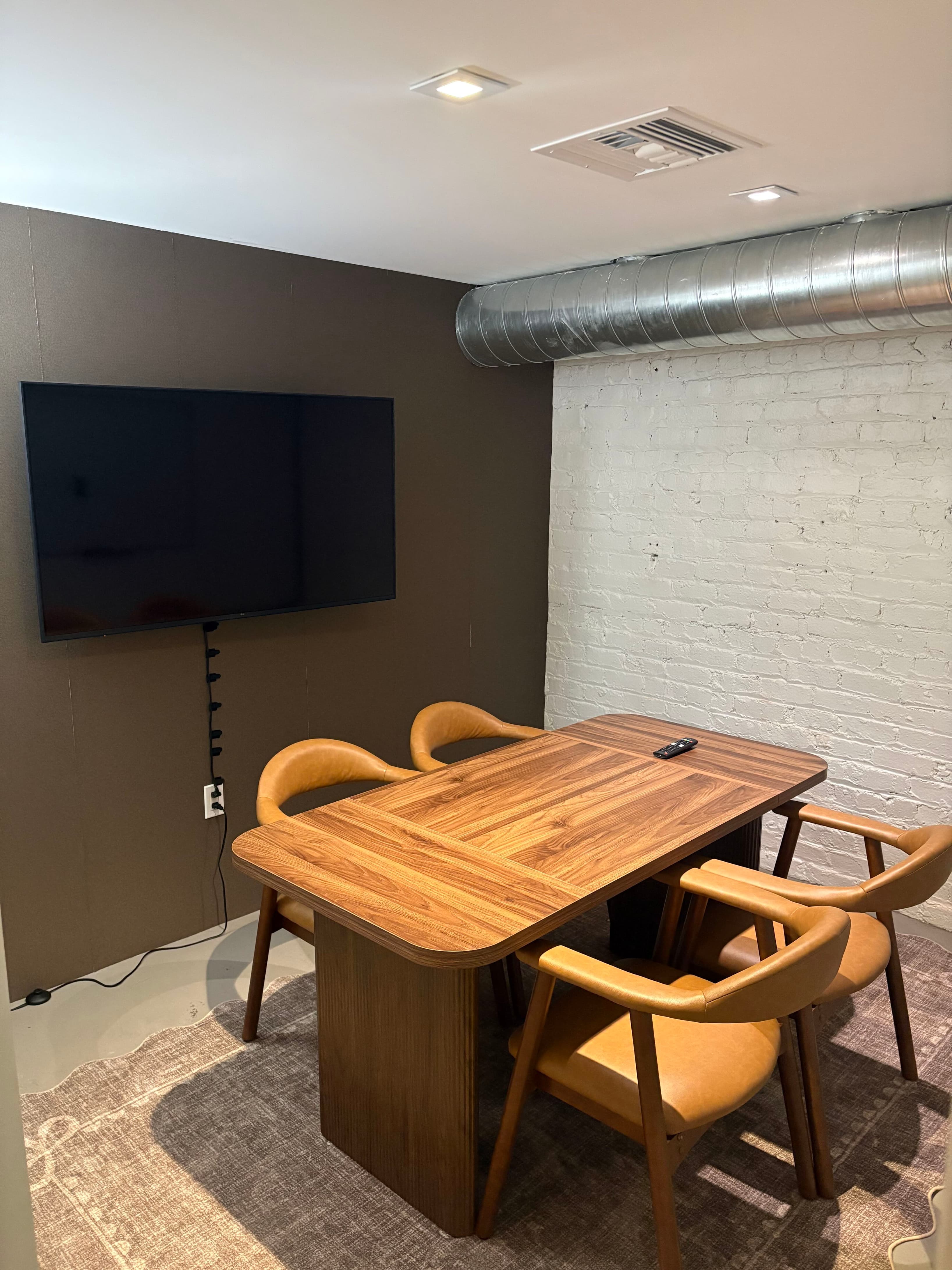 Sleek meeting space with display screen and modern wood table perfect for team presentations and client meetings. Industrial-