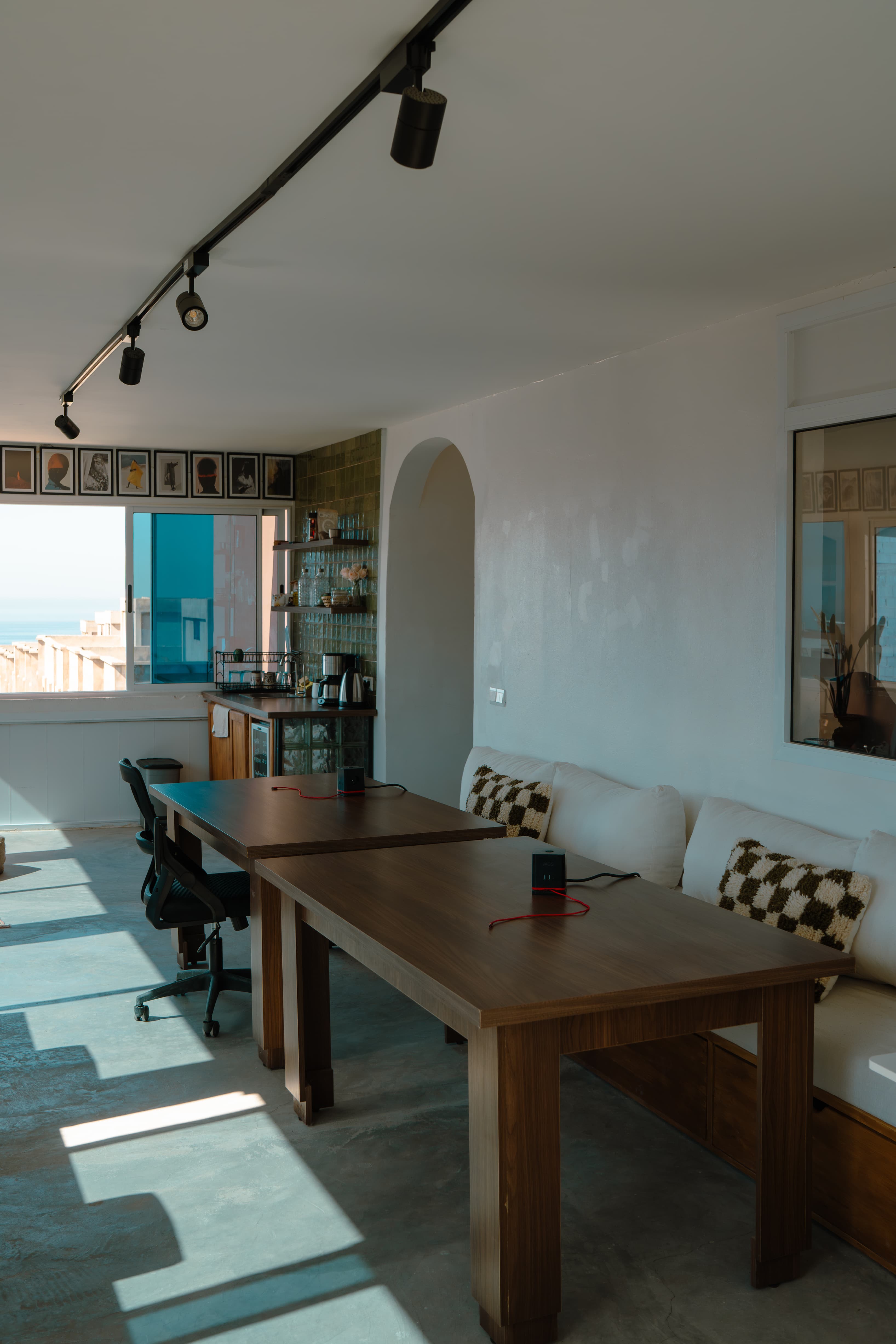 Main coworking area at Amsiln Studio with wooden desks, ergonomic chairs, sofa, natural light, and sea views in Tamraght.