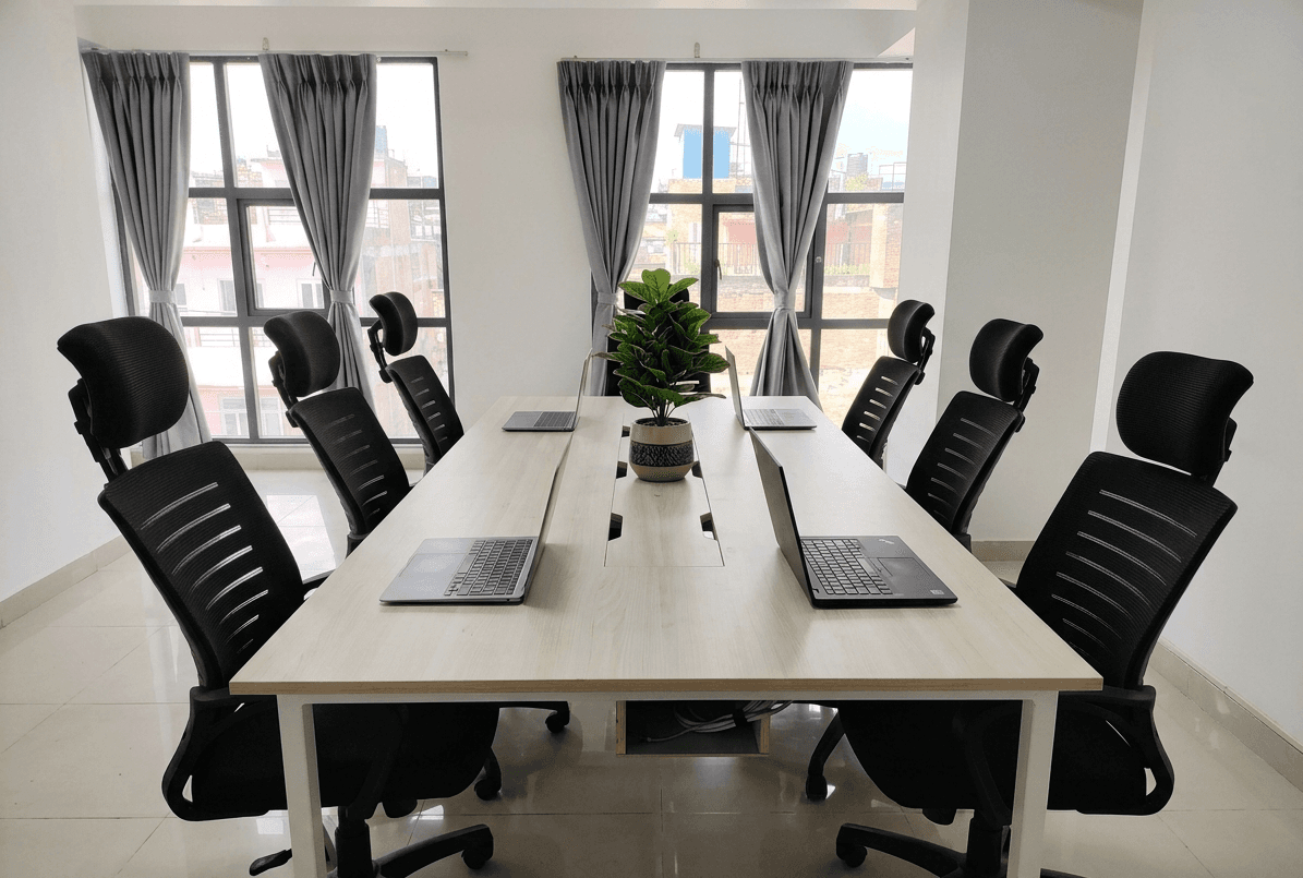 Spacious meeting table with laptops, greenery, and window views — perfect for team discussions. Spacious meeting table with laptops, greenery, and window views — perfect for team discussions.