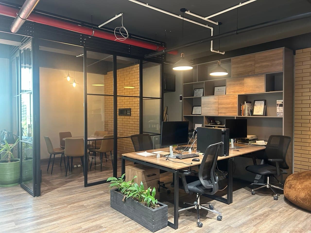 Shared coworking area with dedicated workstations and a private glass meeting room in a modern professional setting. Shared coworking area with dedicated workstations and a private glass meeting room in a modern professional setting.